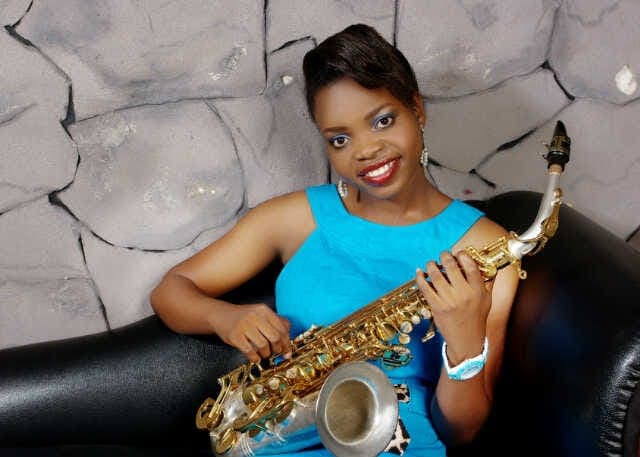 Funmisax in a blue dress, seated with her saxophone