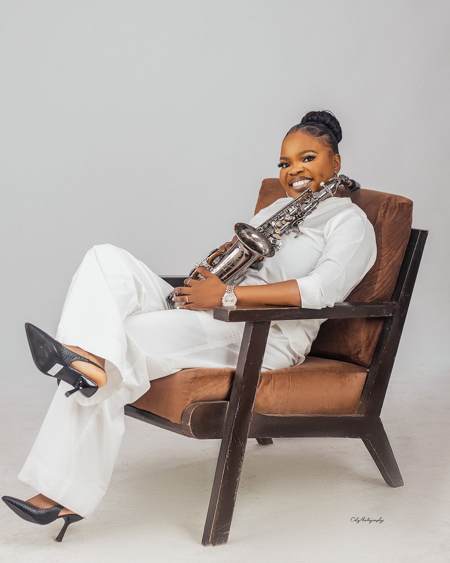 Funmisax seated with her saxophone in a white suit