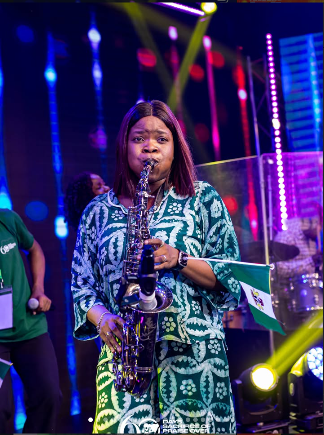 Funmisax playing saxophone on stage with the Nigerian flag